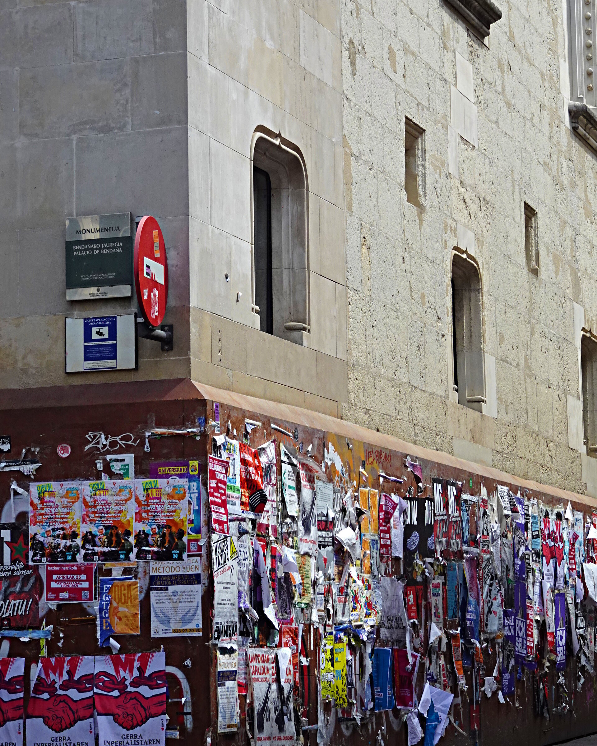 Layers of colourful flyers plastered on a wall below a historic stone building