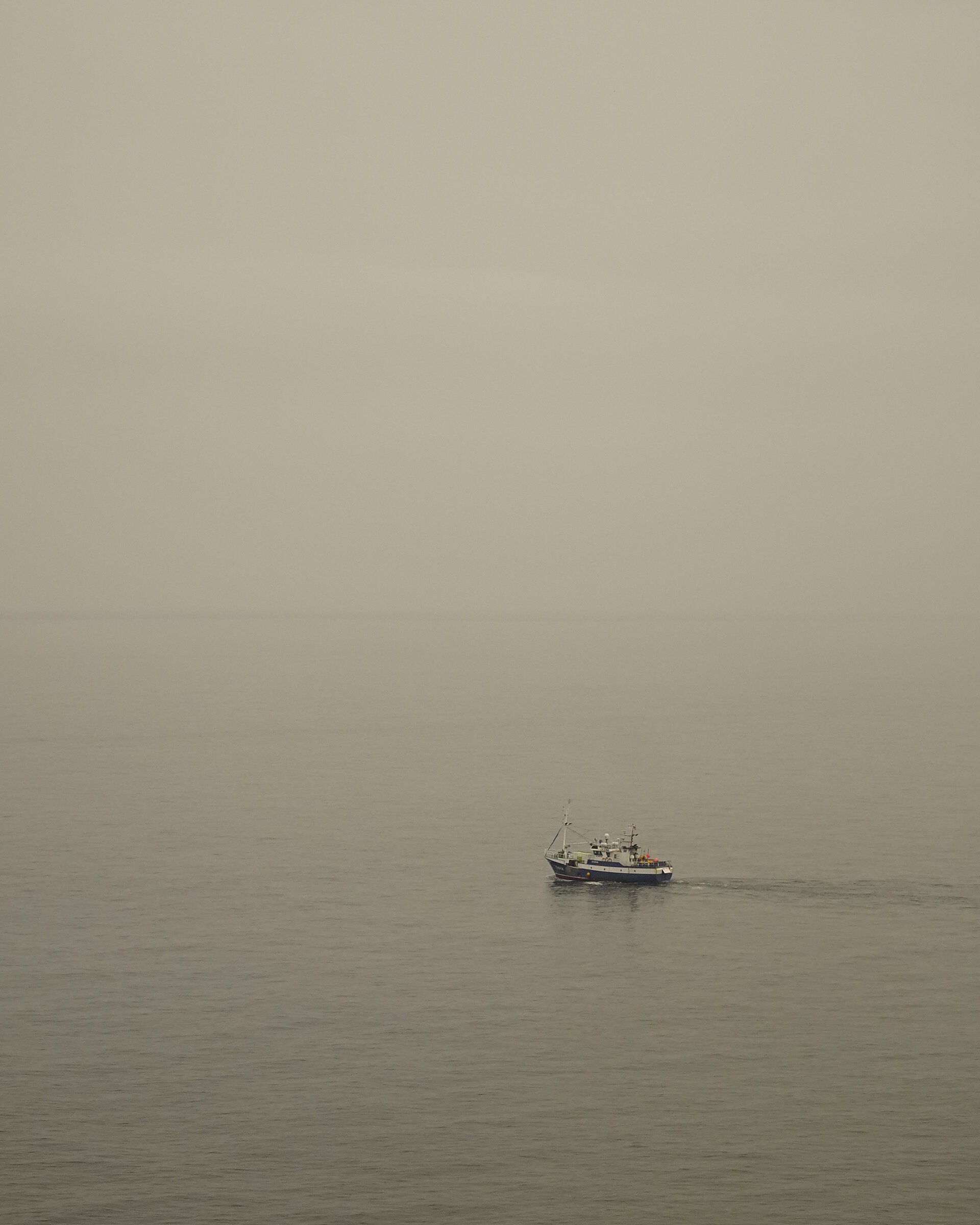 A small boat on hazy calm water under a pale sky