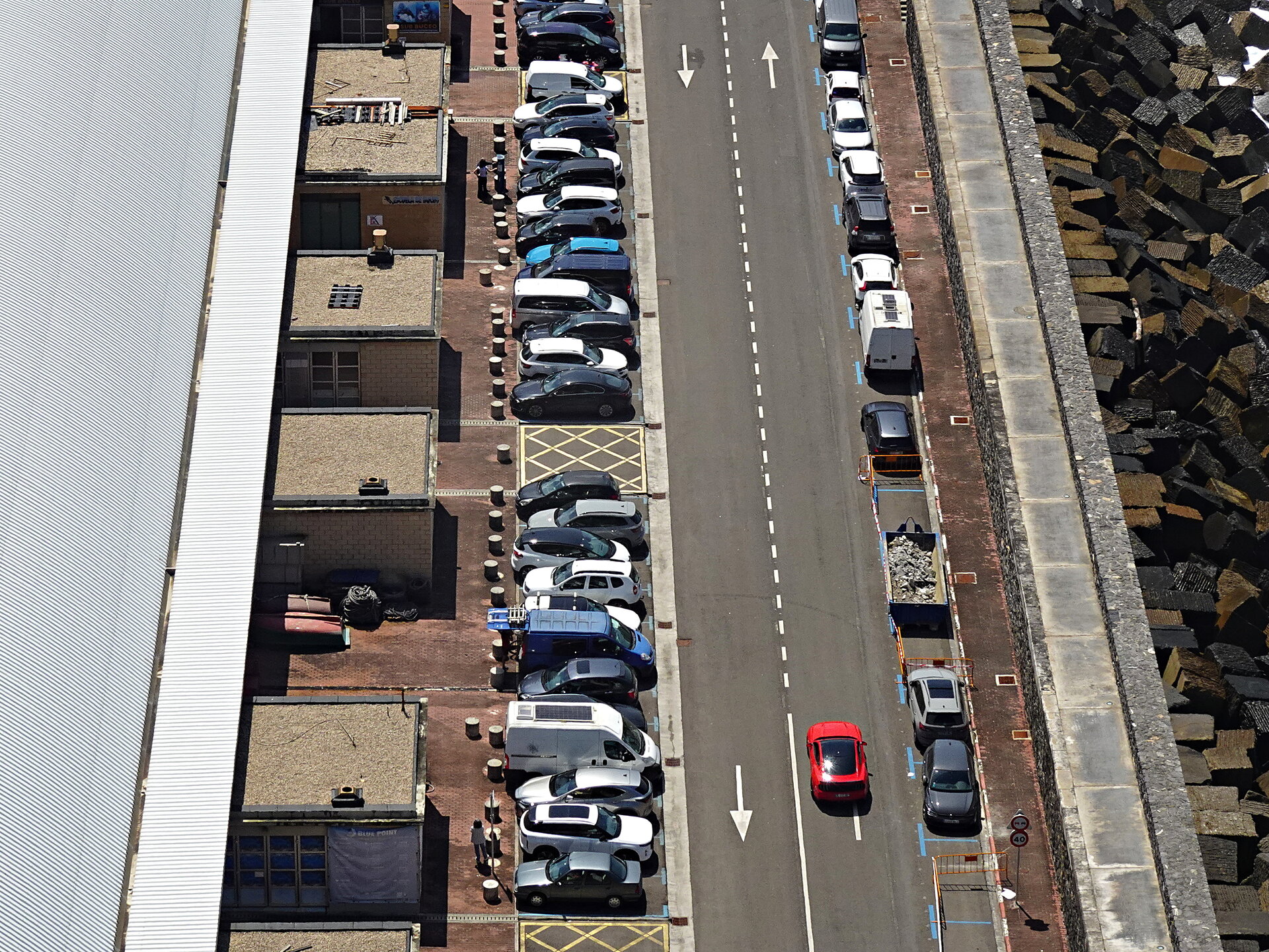 Aerial view down a harbour street lined with parked cars and a single red car