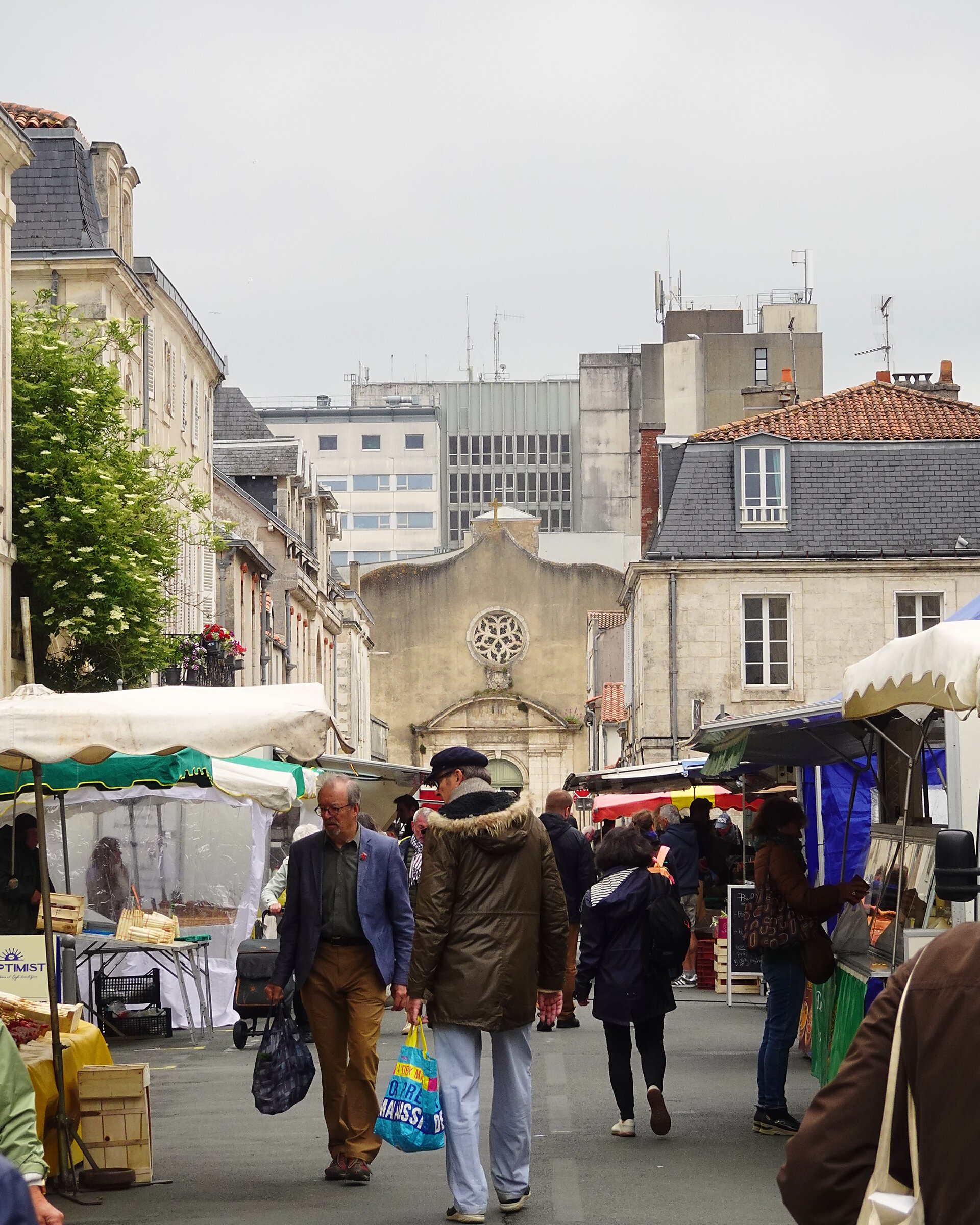 Crowds walking through a busy street market between old buildings
