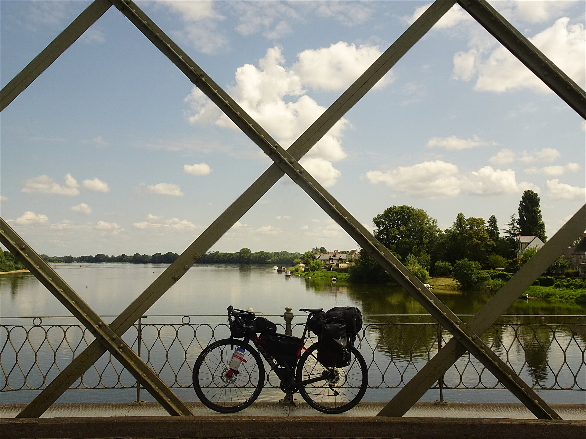 A loaded touring bike on a bridge framed by diagonal girders over a river