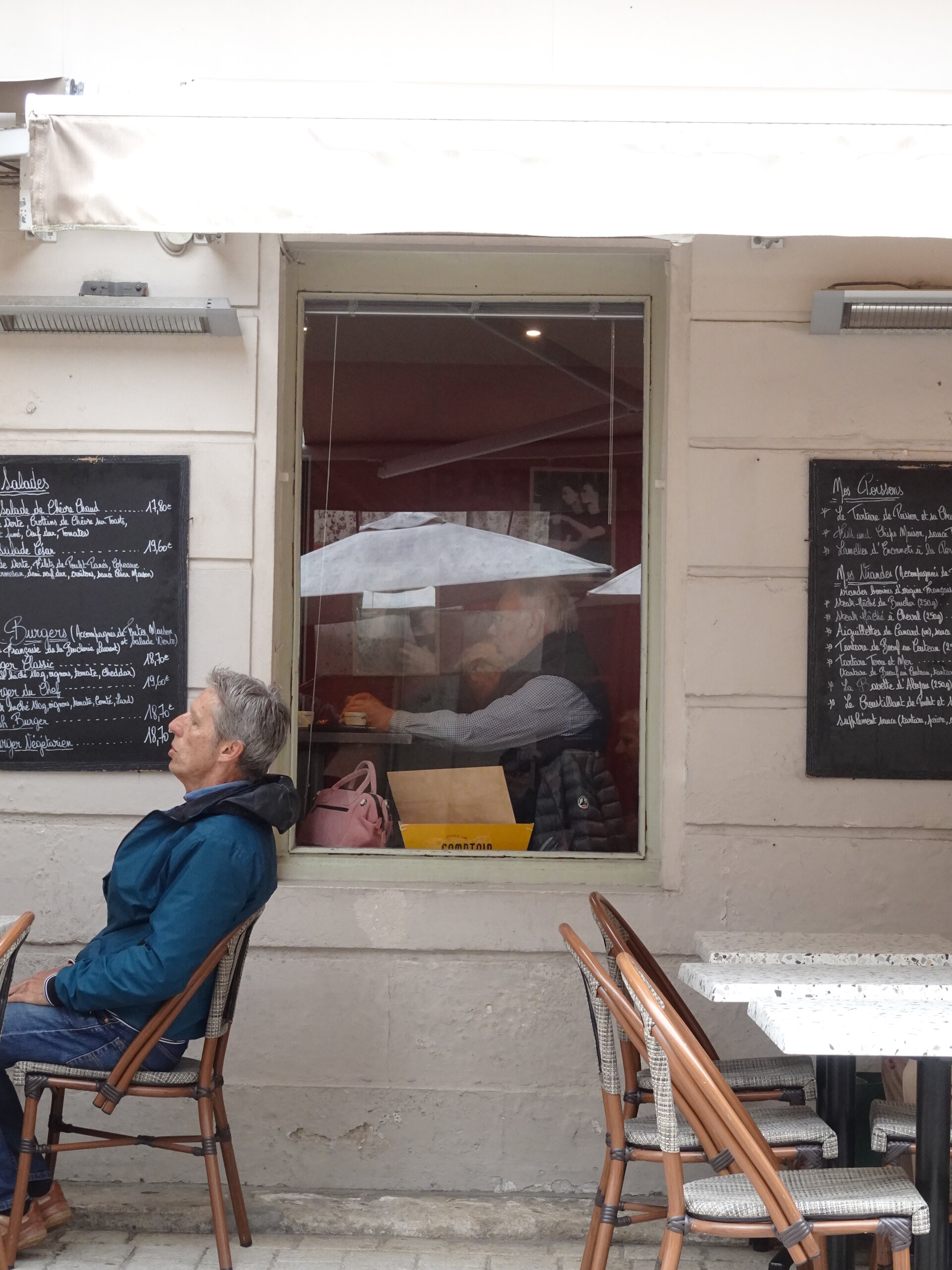 A man sitting outside a café beside chalkboard menus and bistro chairs