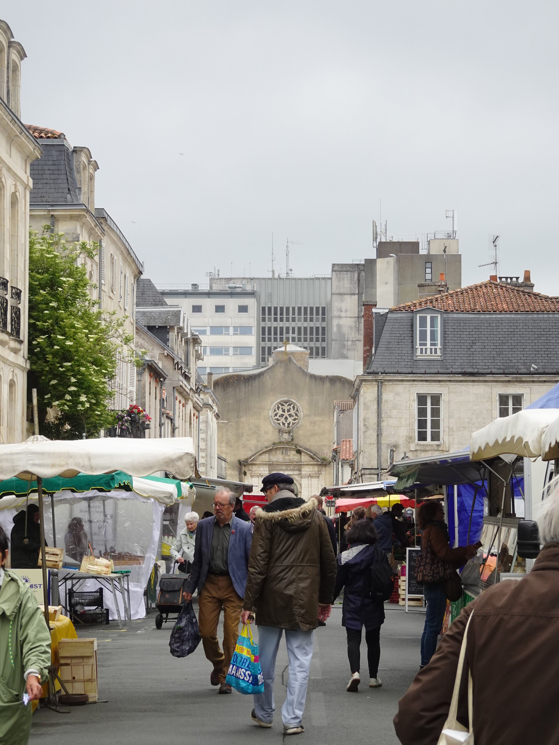 Shoppers walking through a busy street market past old town buildings