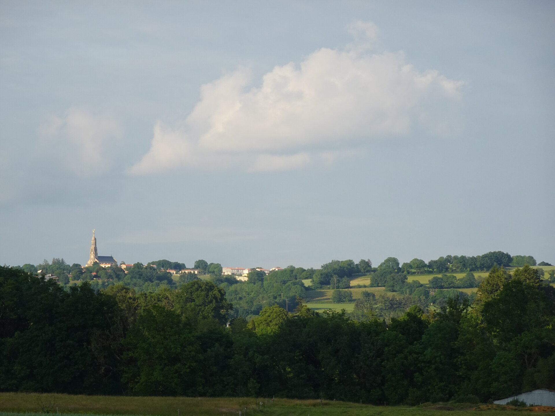 A distant village church spire rising above rolling green countryside