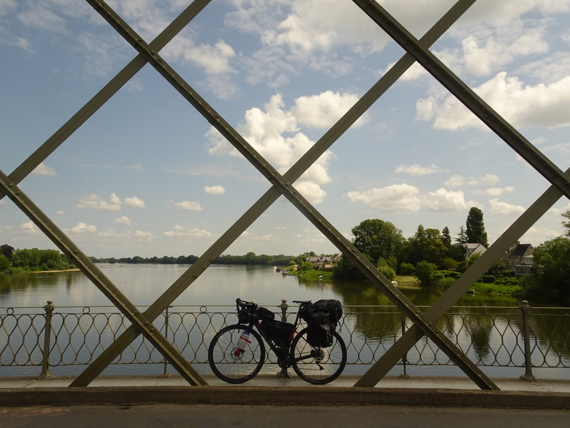 A loaded touring bike on a bridge framed by diagonal girders over a river