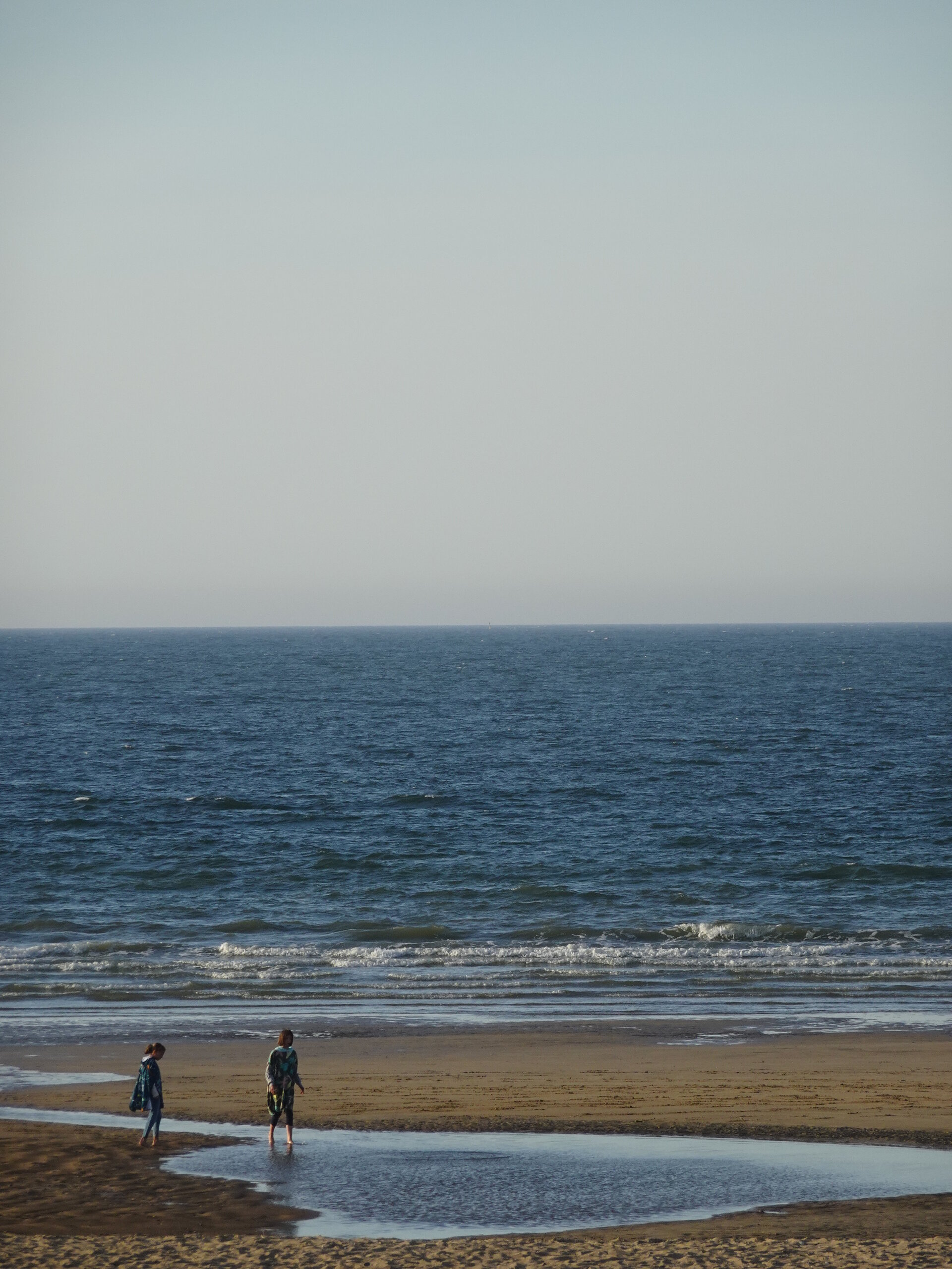 Two people walking on a wide sandy beach beside the sea