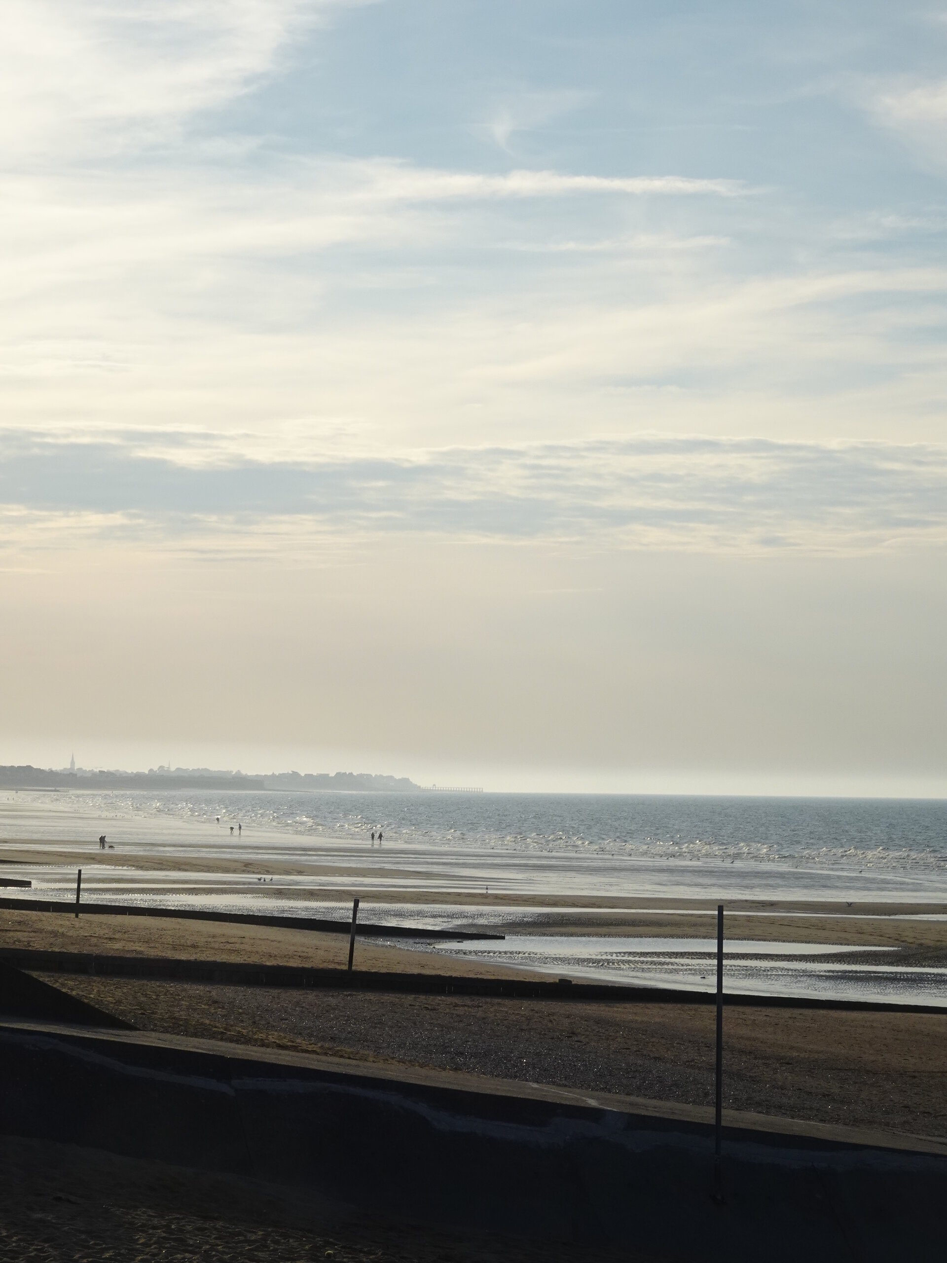 A hazy Normandy beach at low tide under a soft evening sky