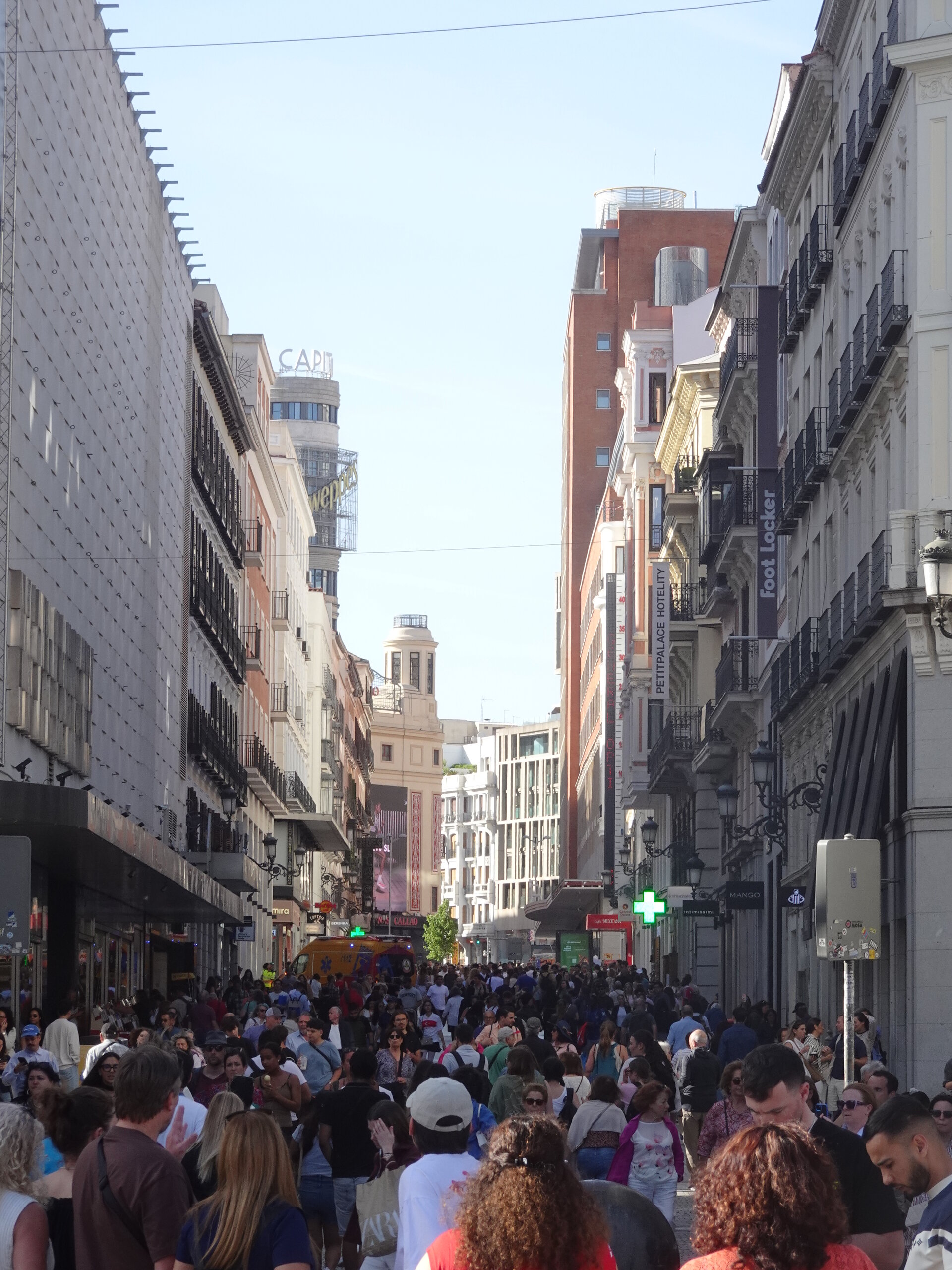Crowds filling a busy Madrid shopping street between tall buildings