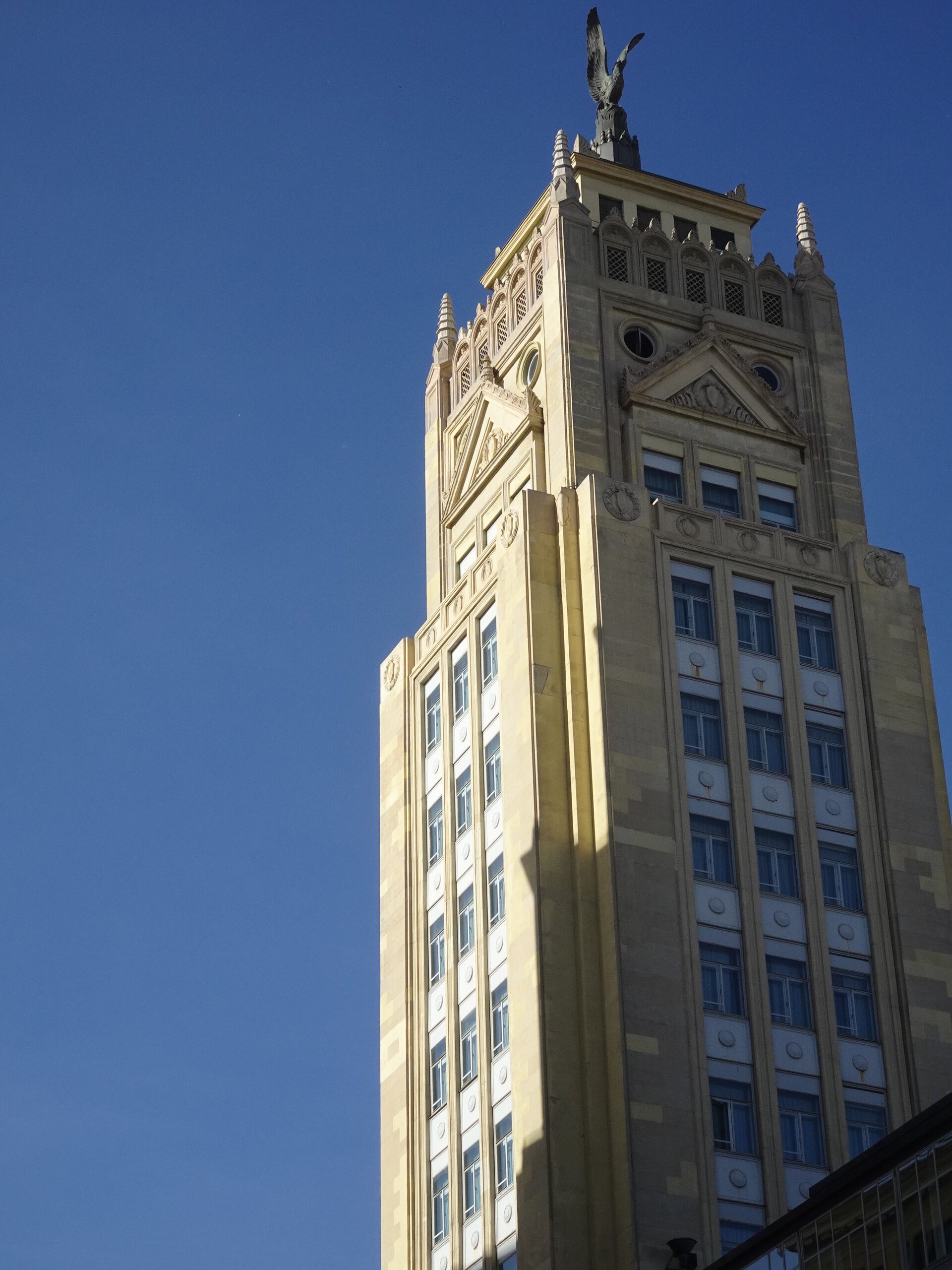 Art deco tower topped with an eagle statue against a deep blue sky