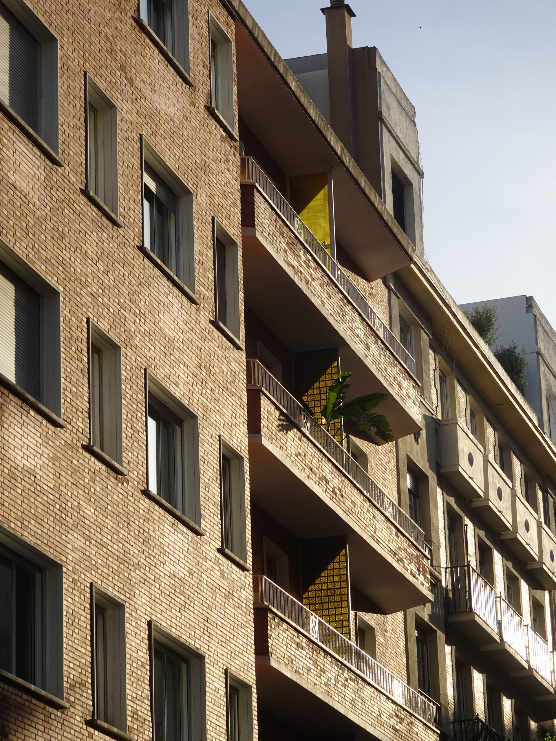 Sunlit brick apartment block with rows of recessed balconies