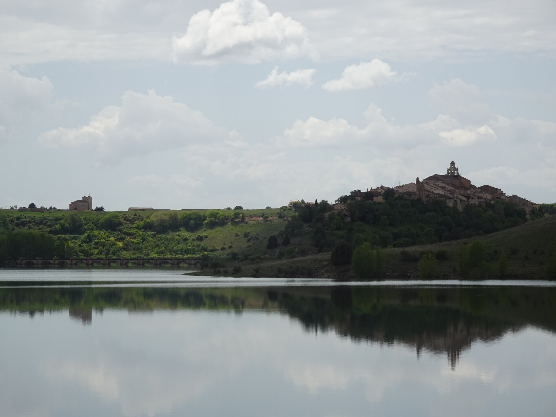 Hilltop town reflected in a calm reservoir beside an old arched bridge