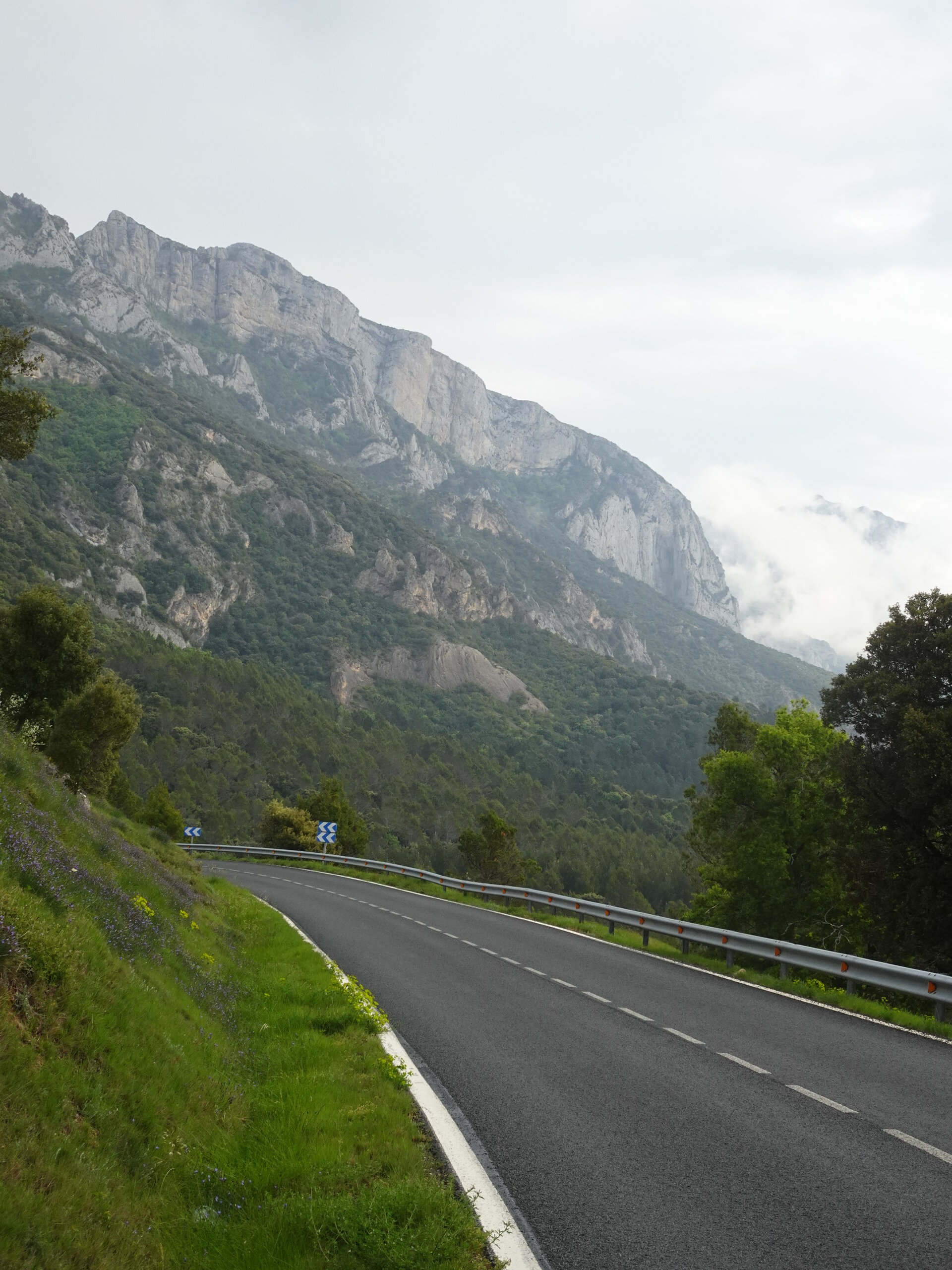 Empty road curving below steep grey limestone mountains
