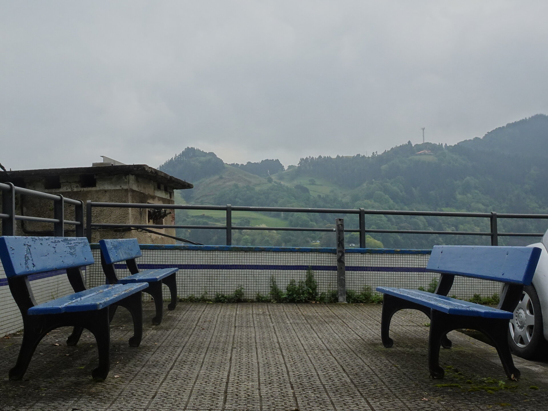Weathered blue benches on a tiled terrace overlooking green Basque hills