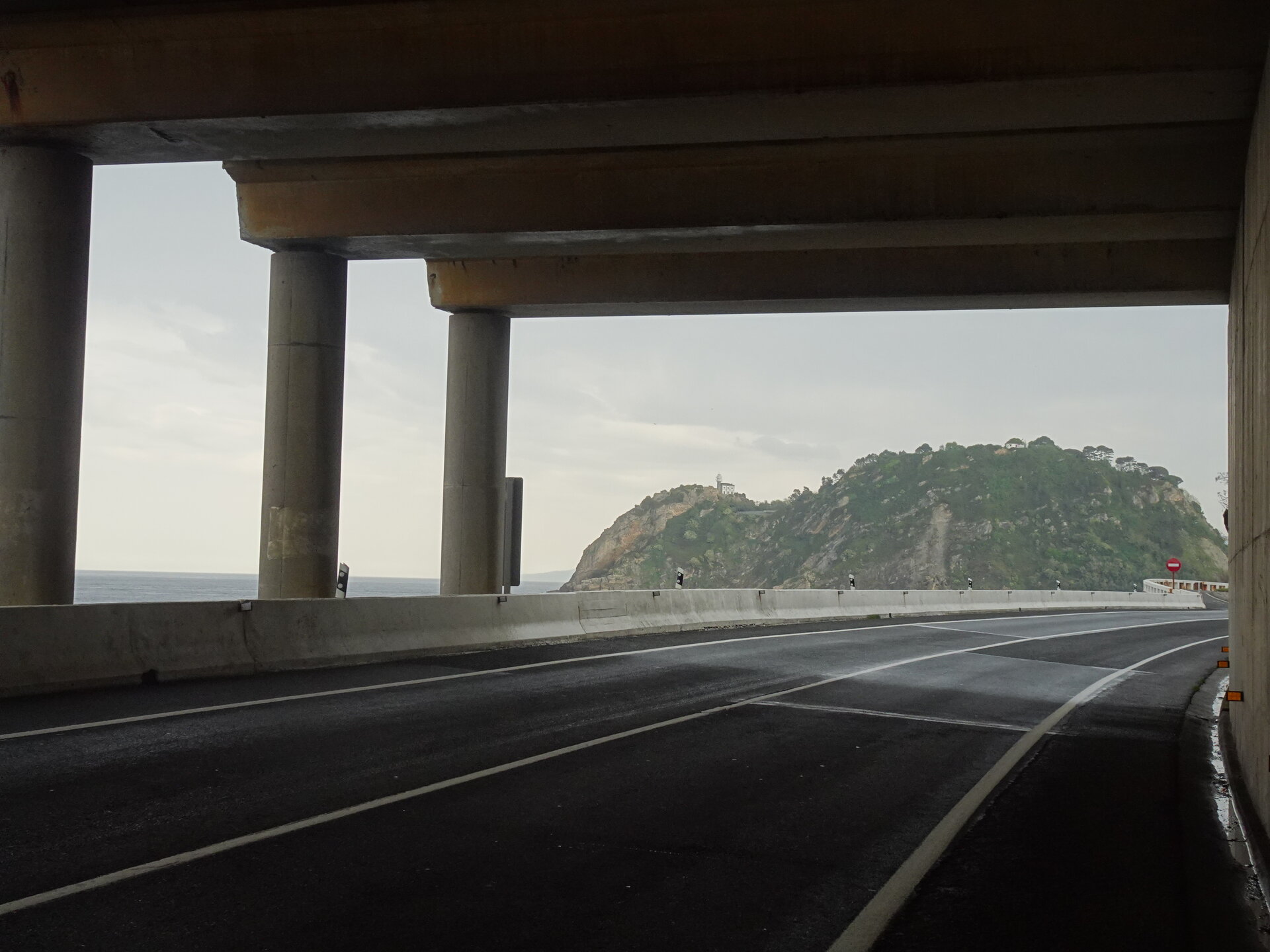 Coast road passing under a concrete flyover with a headland and sea beyond