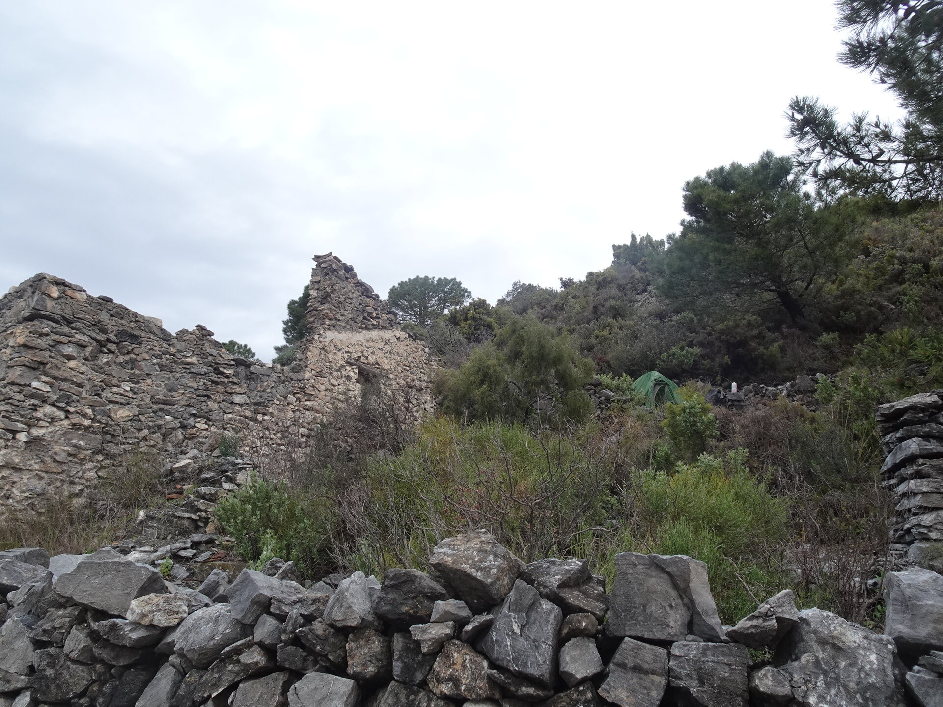 Stone ruins and a green tent pitched behind a dry stone wall on a scrubby hillside