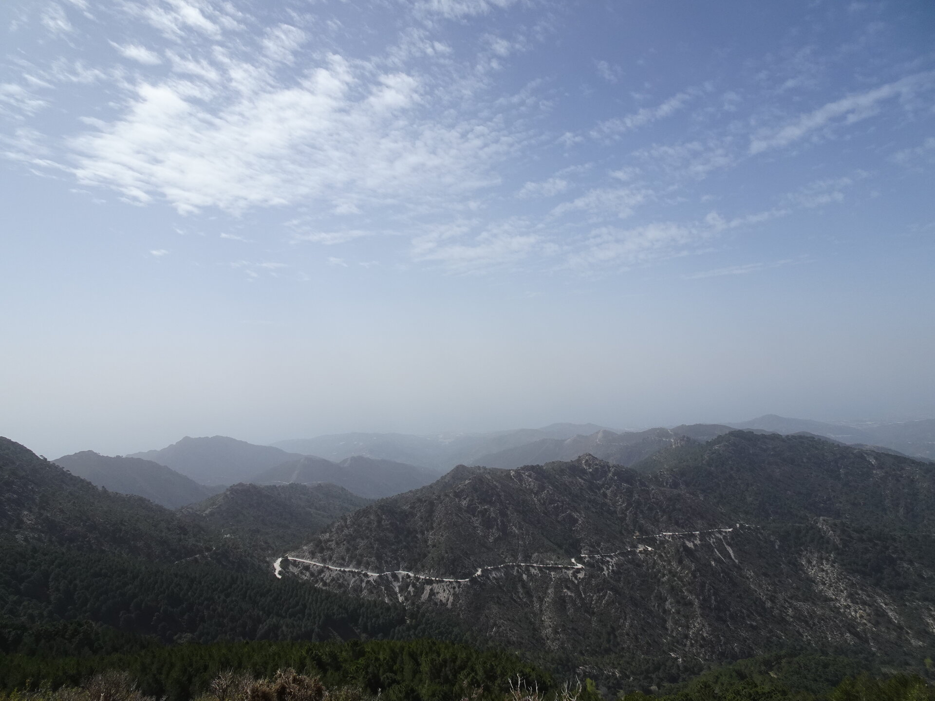 Winding mountain road switchbacking through forested ridges with the Mediterranean hazy beyond