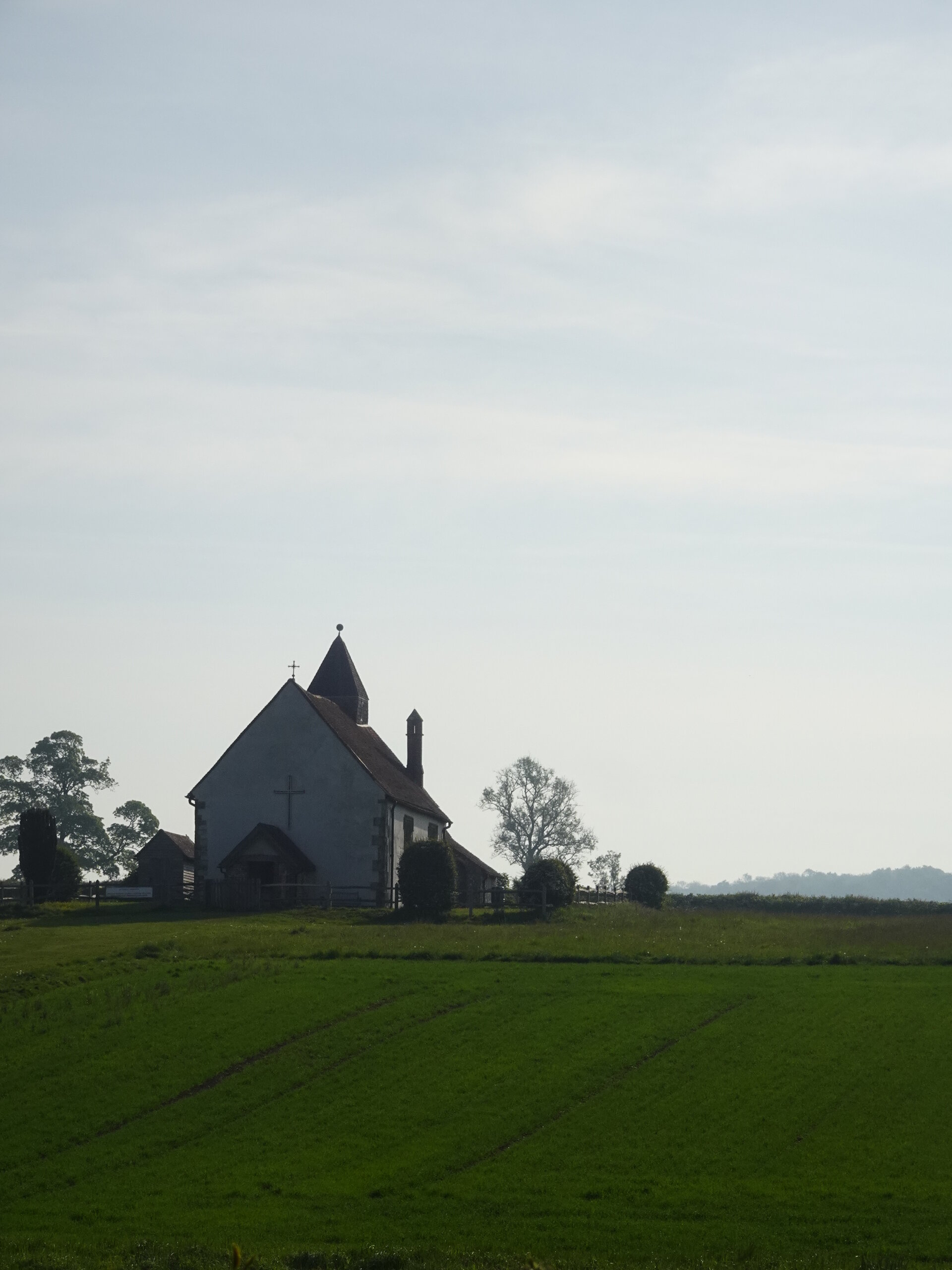 A small white hilltop church above a green field under a pale sky