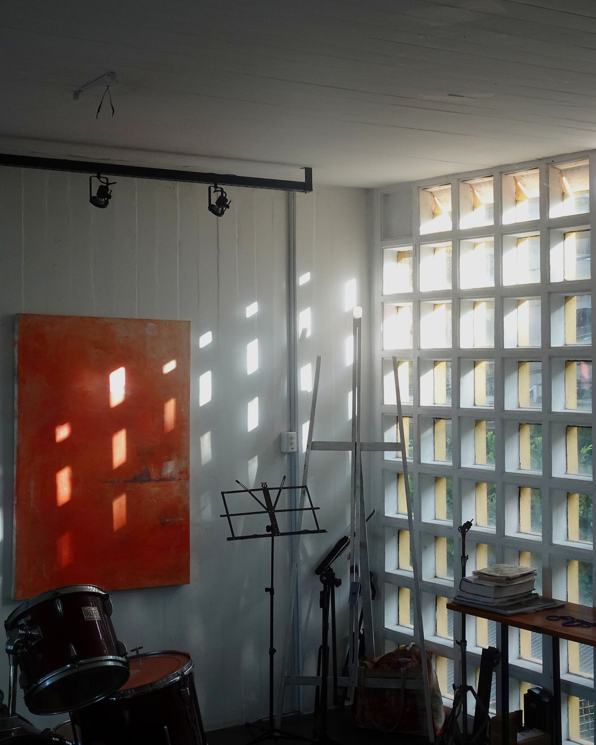 Sunlight through a glass-block wall falling on a red painting and a drum kit