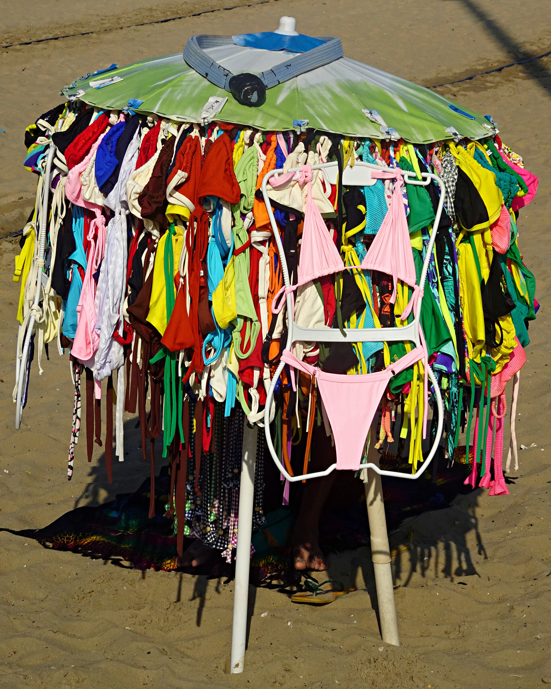 A beach parasol hung with dozens of brightly coloured bikinis for sale