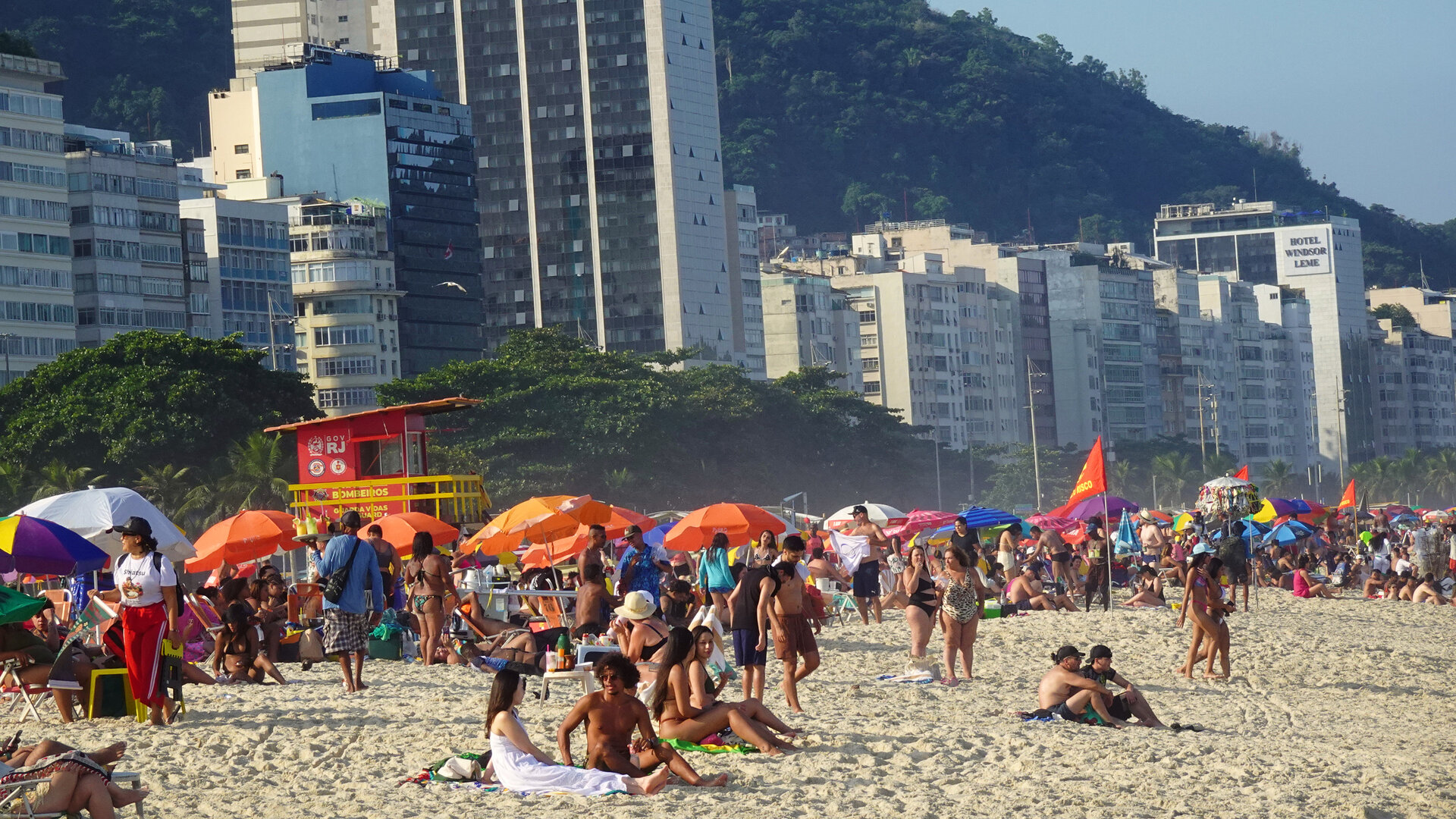 Crowded Copacabana sand with orange parasols below a wall of apartment towers