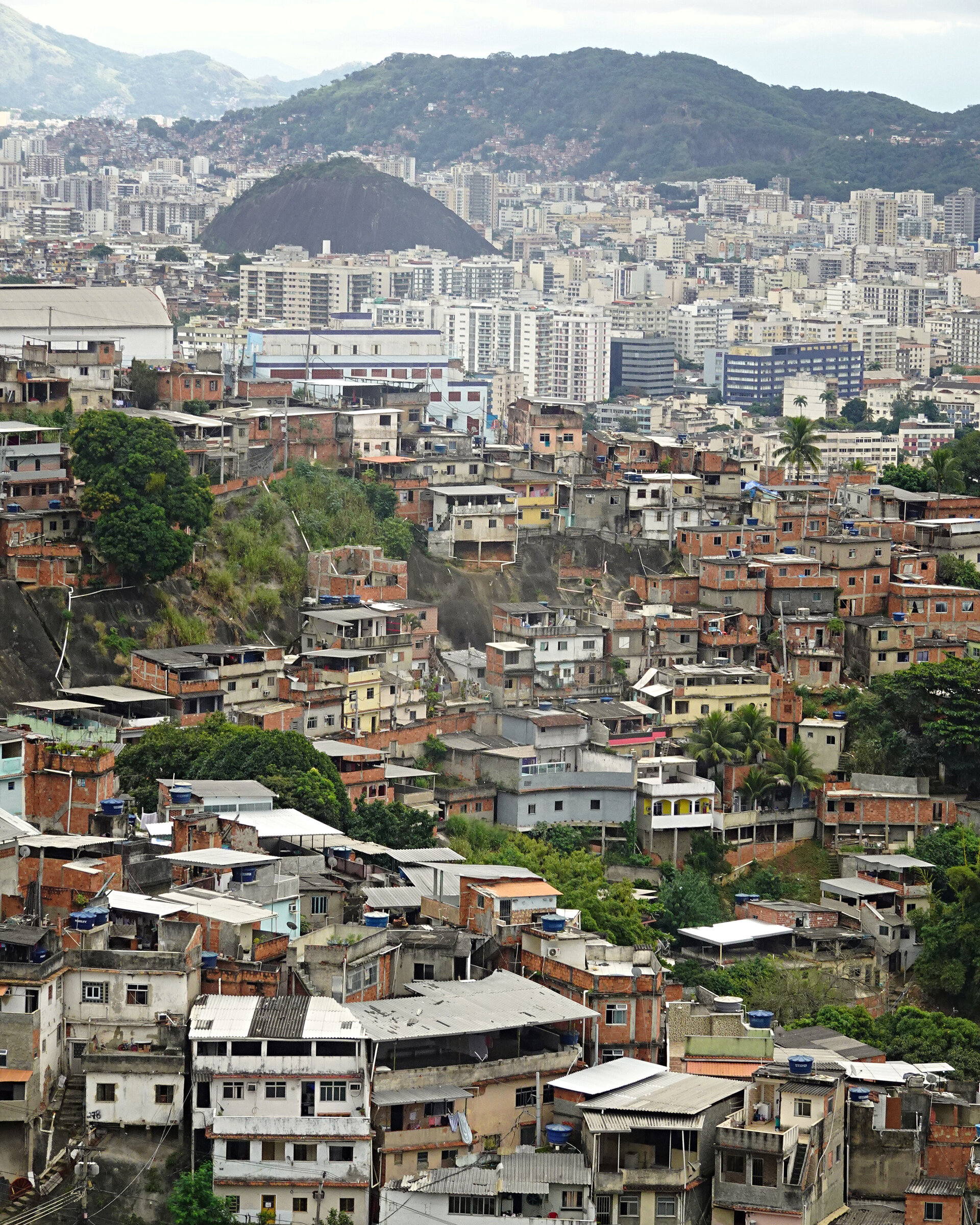 A favela of stacked brick houses on a hillside with the city and hills beyond