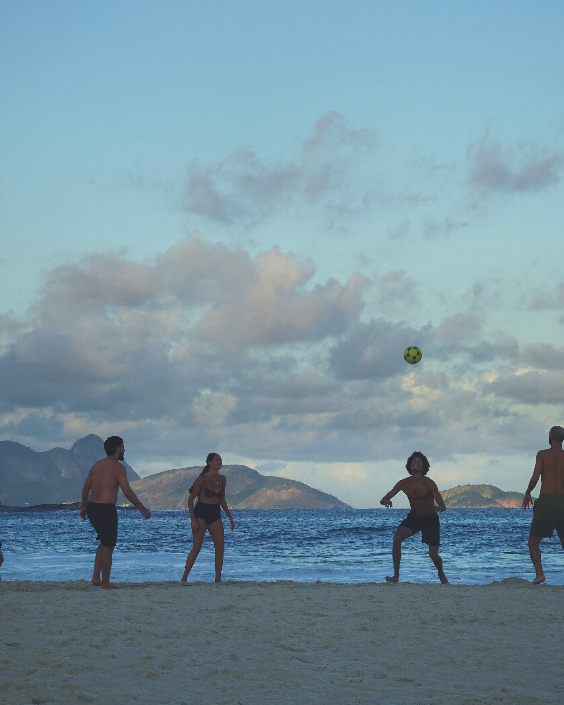 Altinho at dusk: a football hangs in the sky above players at the water's edge
