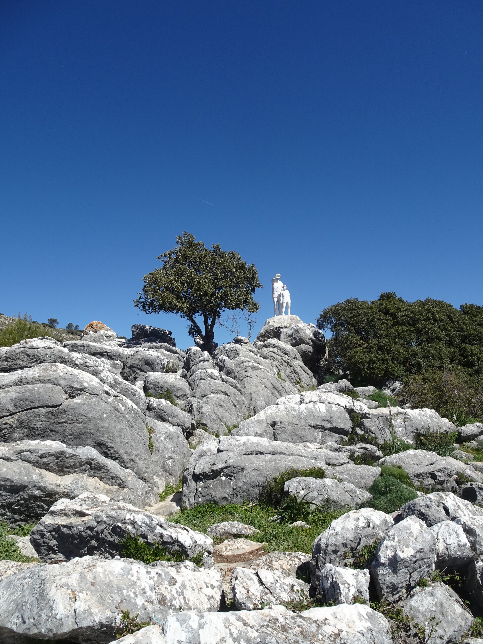 White statue on a rocky limestone hilltop under blue sky