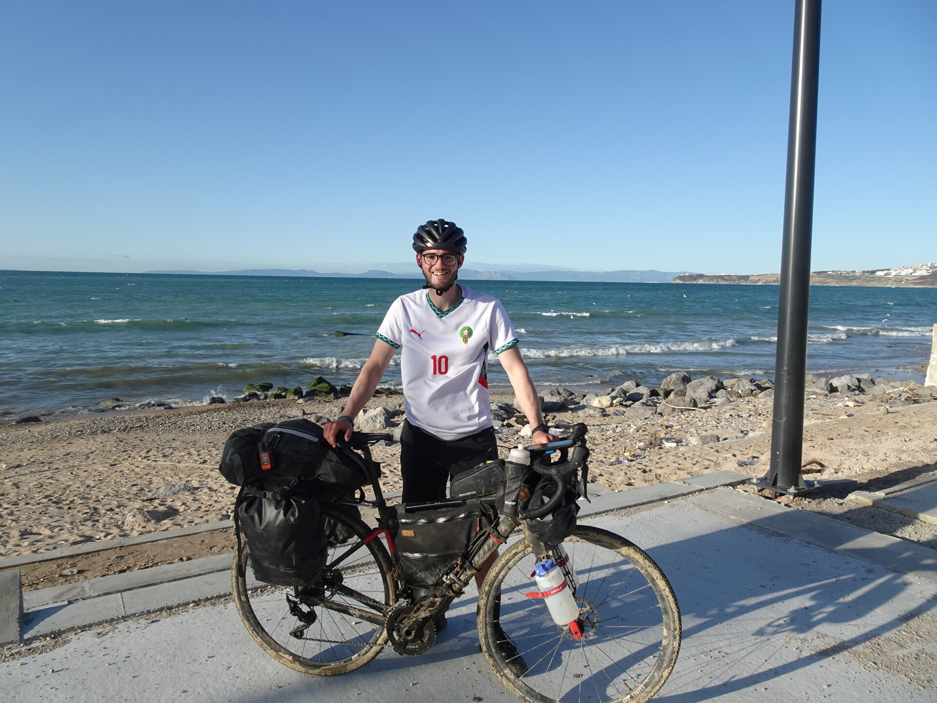 Cyclist with loaded touring bike on Tangier beach with Spain across the strait