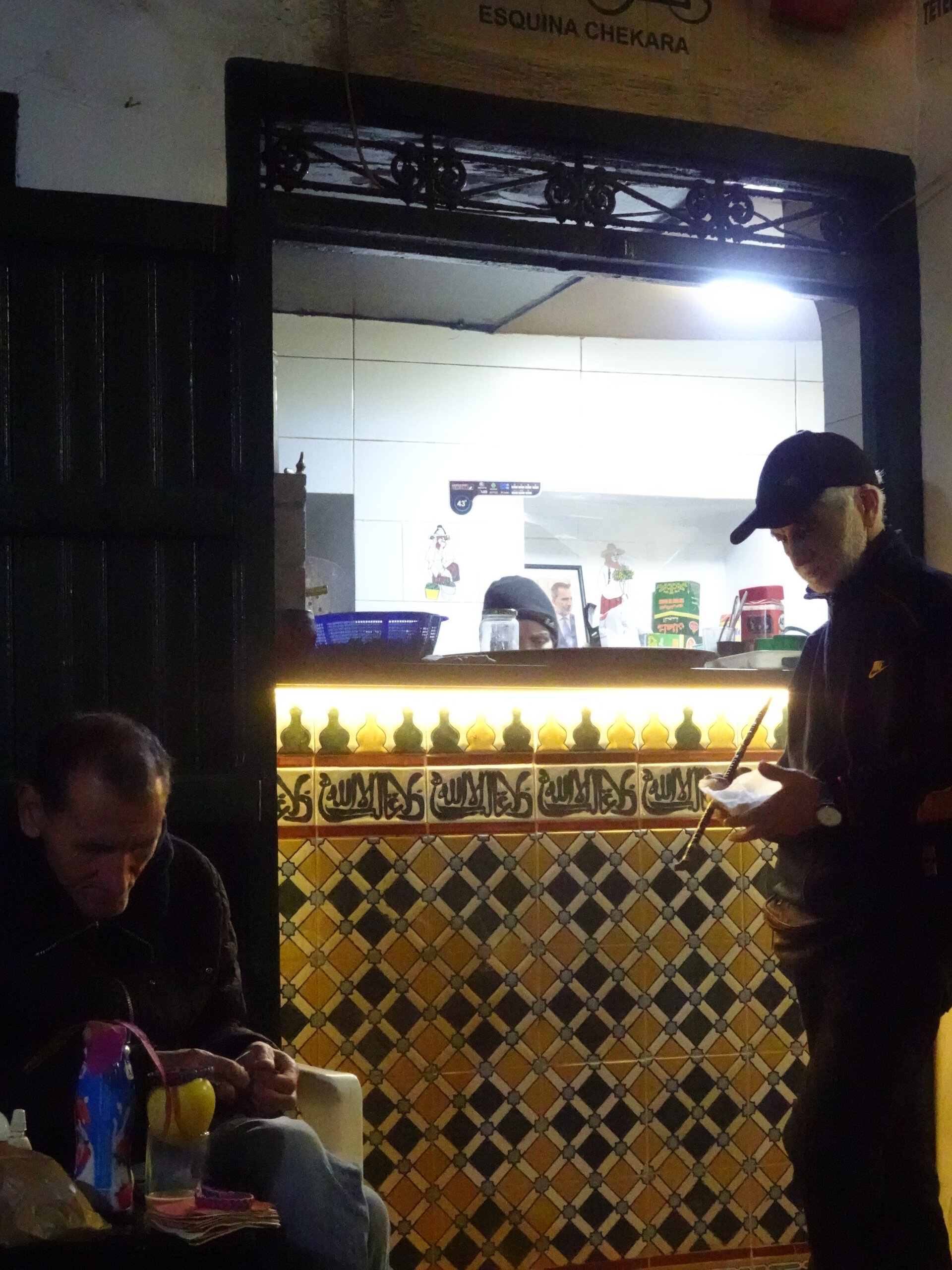 Man reading beside an Arabic-tiled cafe counter at night