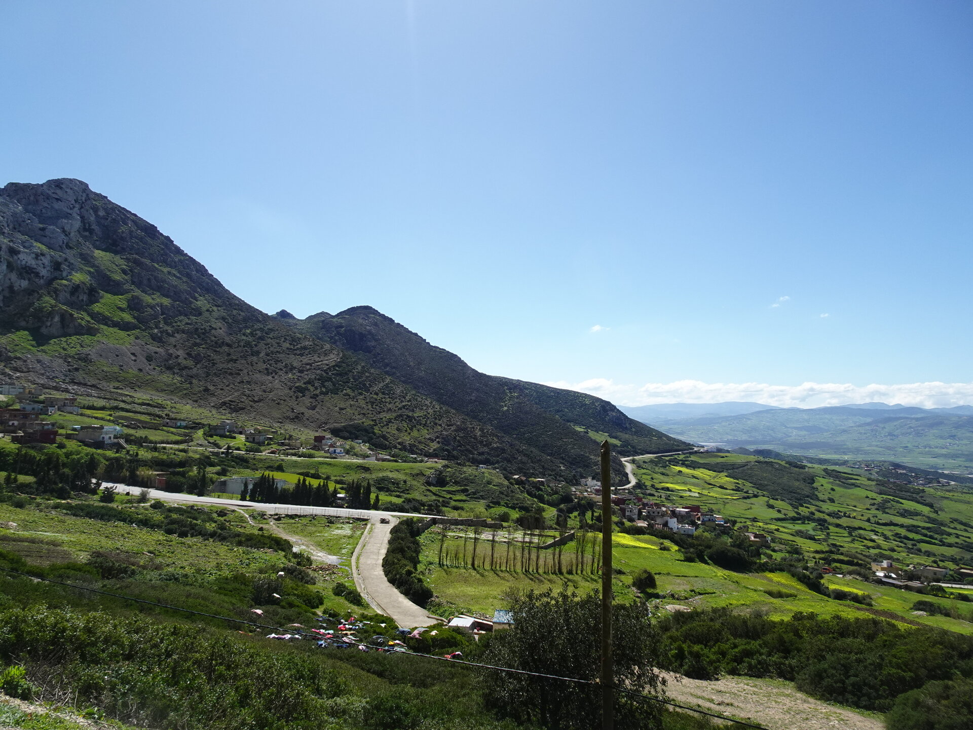 Winding road through green valley beneath a rocky mountain peak