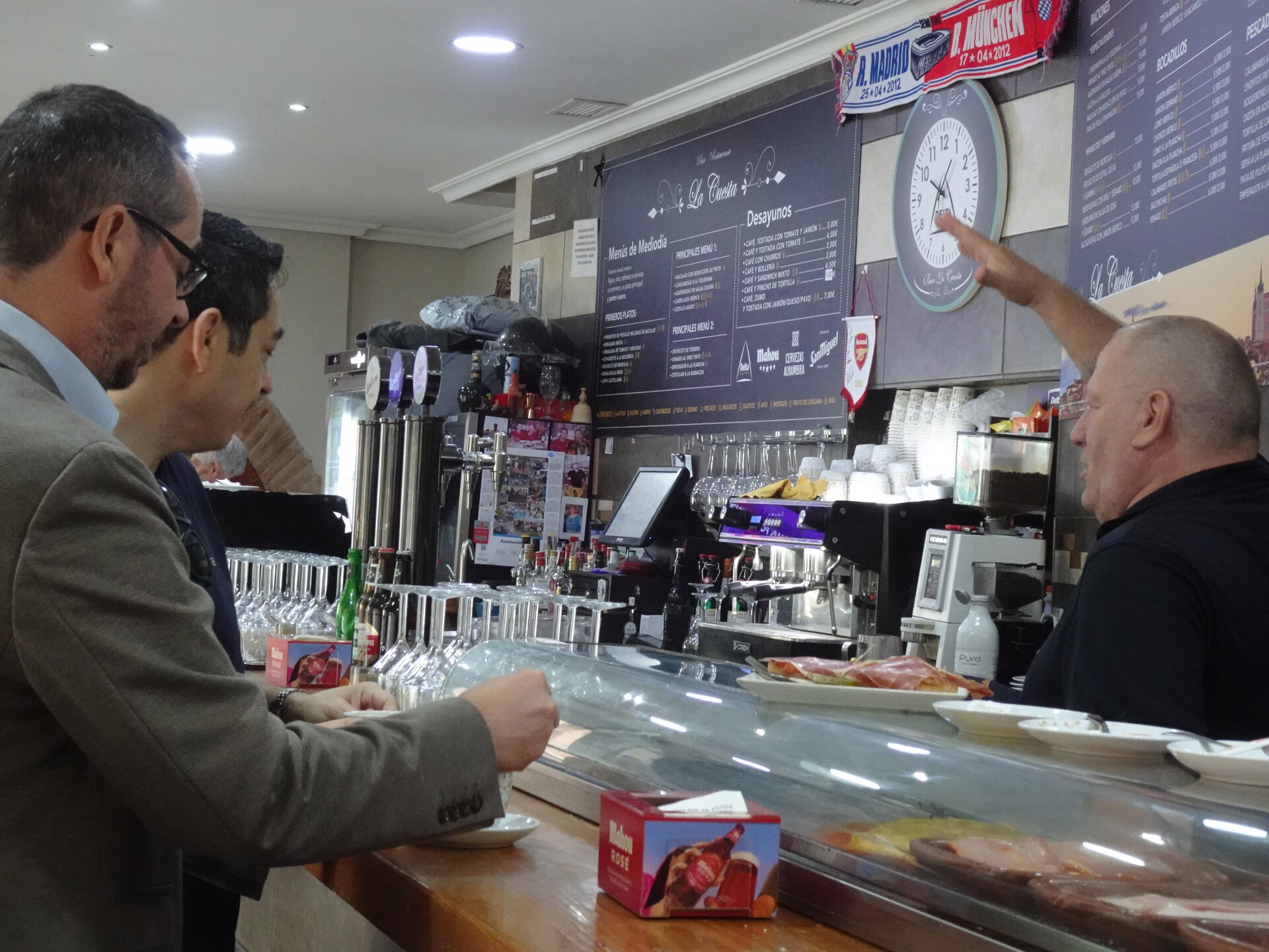 Two customers at a tiled bar counter as the barman gestures behind the taps