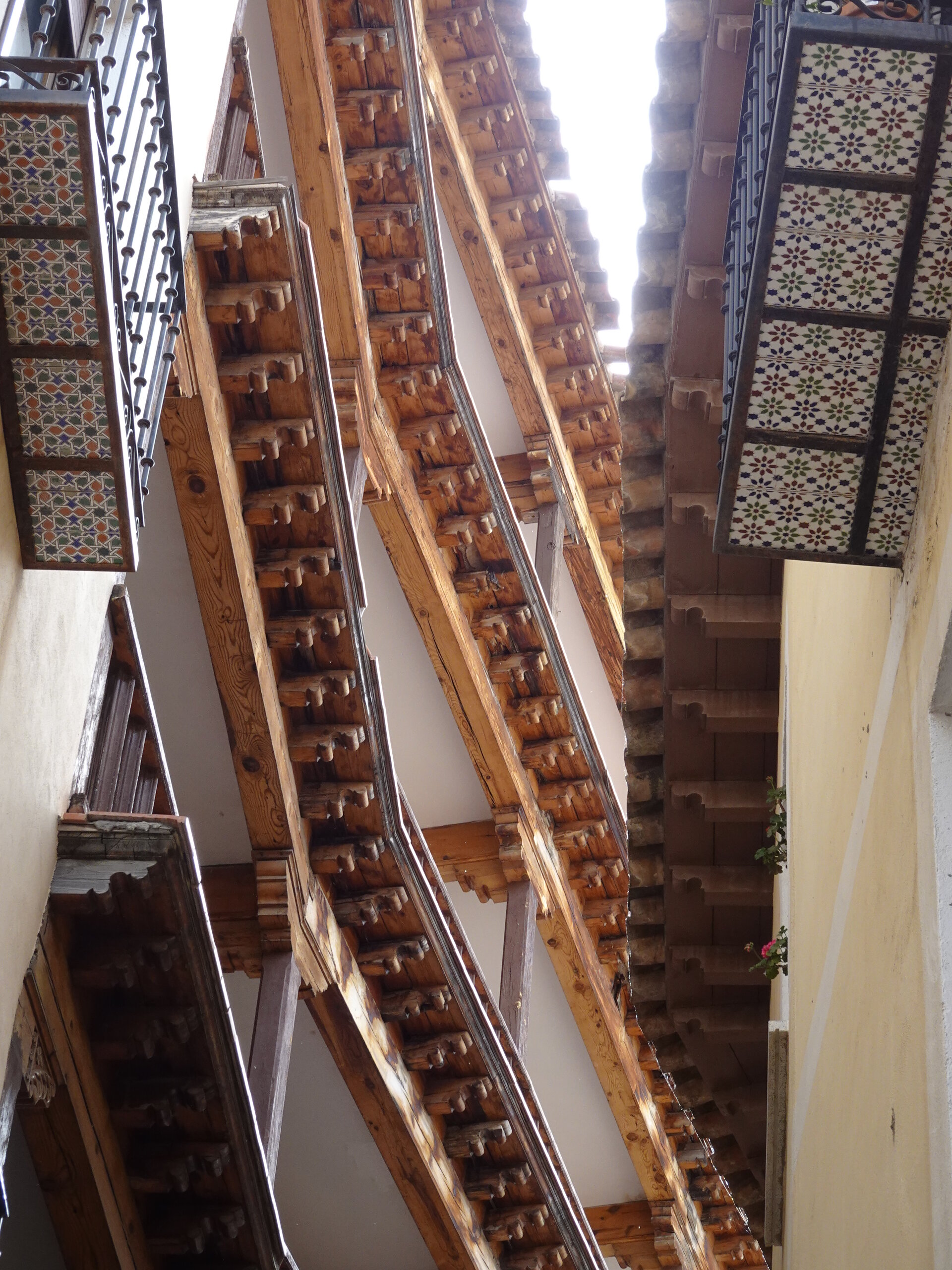 Looking up at carved wooden eaves and patterned tile soffits between old houses